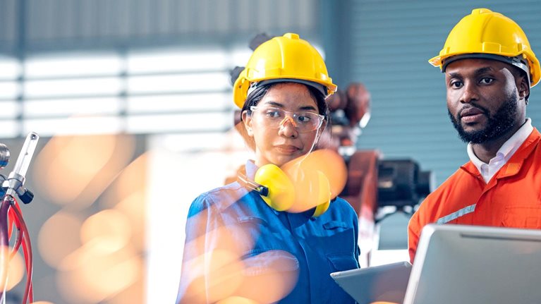 Two engineers having a meeting in front of industrial robots welder in production line.