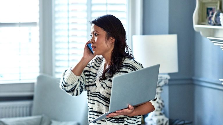 Woman holding laptop and listening on smartphone