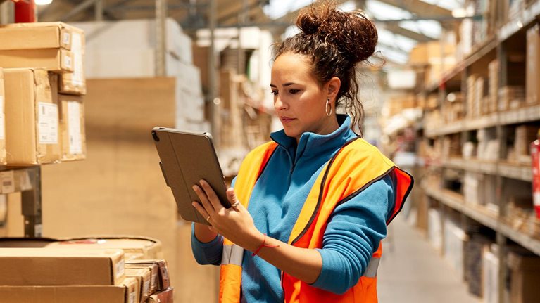 A warehouse worker takes inventory in the storage room standing next to a shelf and using a digital tablet. - stock photo