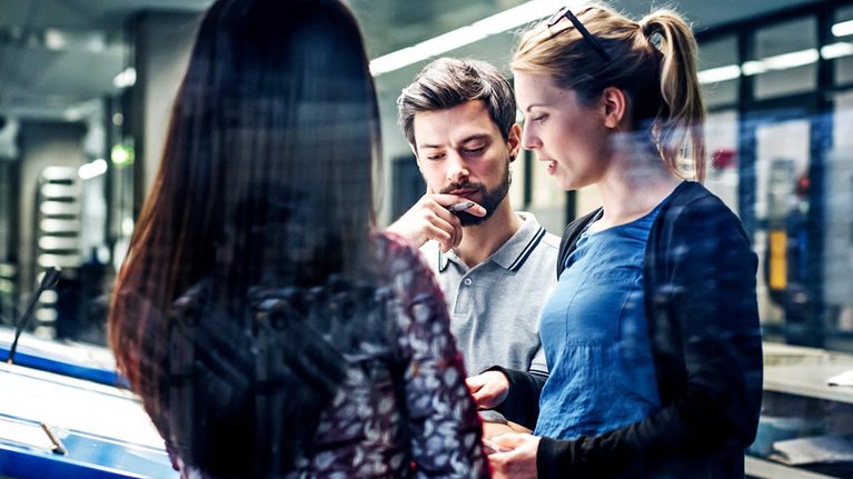 A group of printing plant engineers talking and working together at a large console