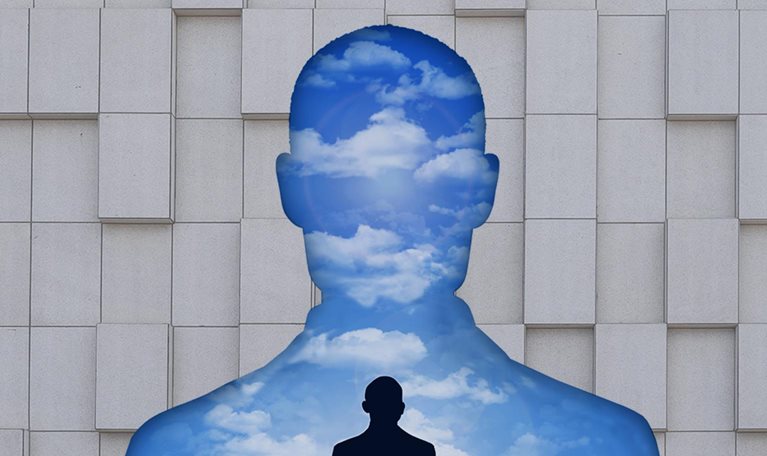 A silhouette of an executive's torso creates a cutout in a corporate wall, filled with a landscape that predominantly features the sky. In that landscape, a smaller silhouetted figure sits on the ground, lost in deep contemplation.