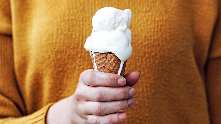 Woman in yellow sweater holding a melting ice cream cone in her hand