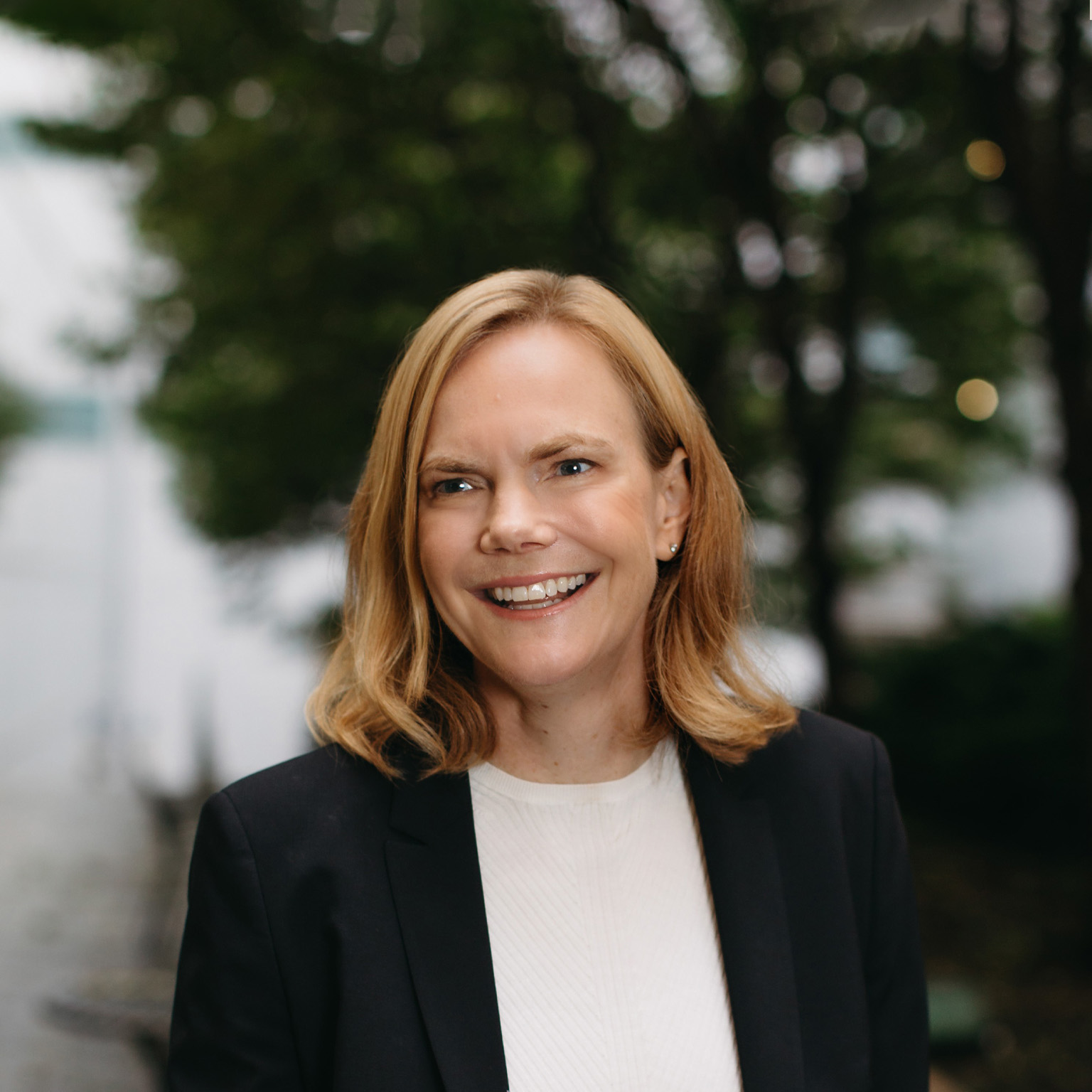 Portrait of a smiling Janet Bannister with an outdoor setting as a blurred background.