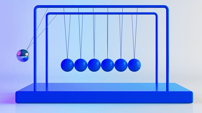 Newton's Cradle, with shiny, metallic balancing balls. Six remain still as one is in motion.