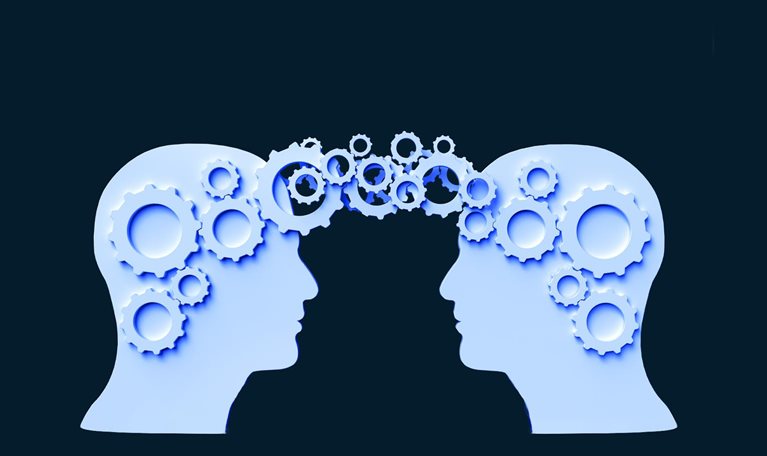 Two silhouettes of human heads face each other against a dark background. Gears of various sizes connect between the two heads, symbolizing the exchange of ideas and collaboration.