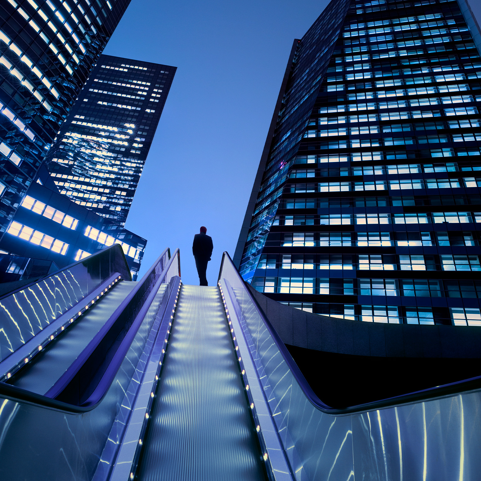 Businessman on top of moving escalator at illuminated business district - stock photo