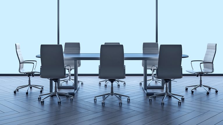 A modern boardroom table and chairs with large windowpanes behind it.
