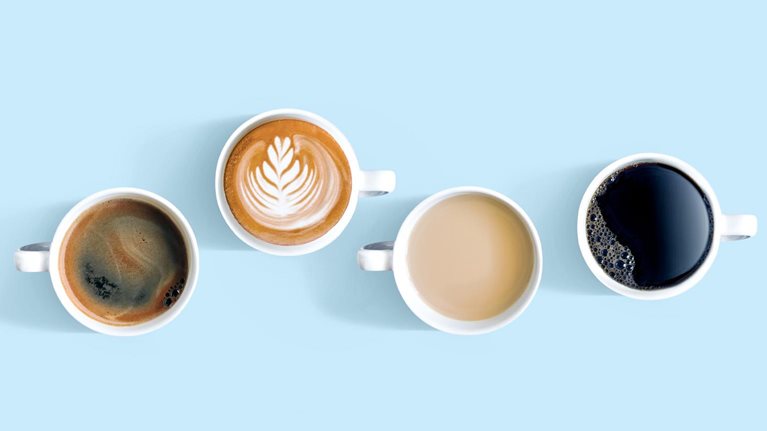 Overhead view of cups with different types of coffee. One of the cups sits higher up in the frame with a foam flourish on top.