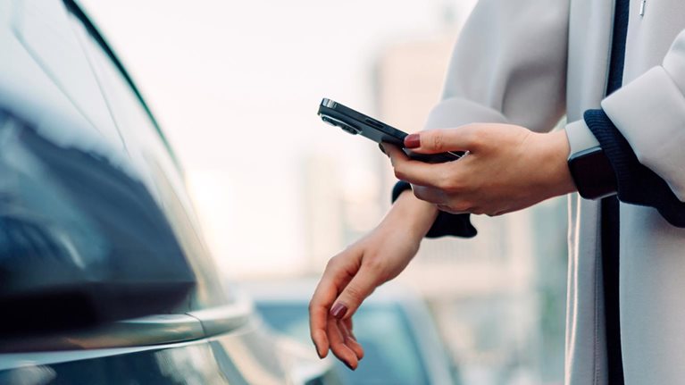Close up of young Asian woman using mobile app device on smartphone to unlock the doors of her intelligence car in city street