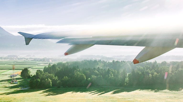 View of lush green fields outside plane window as wing flies forward.