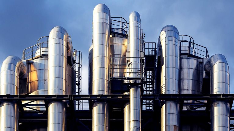 Image of interwoven chemical pipes at a factory shining in the sunset.