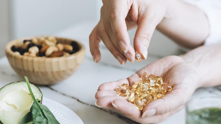 Woman Doctor Nutritionist Hands In White With Omega 3, Vitamin D Capsules With Green Vegan Food