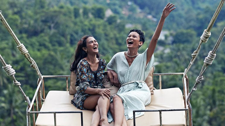 Two women sit on a swing enjoying jungle views while on vacation