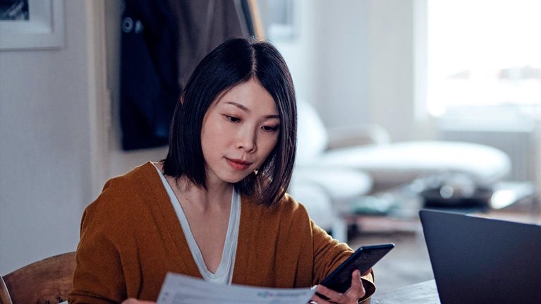 A man and woman handling forms with a phone and laptop on hand