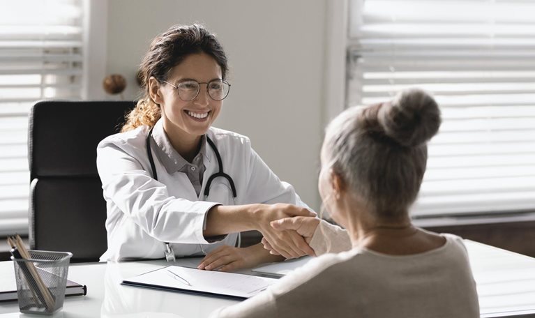 Young Hispanic female doctor shaking hand of senior woman patient