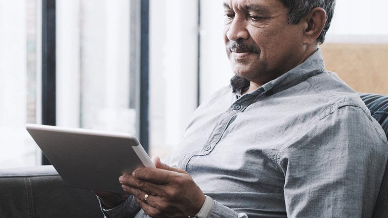 Senior man using a digital tablet on the sofa at home.