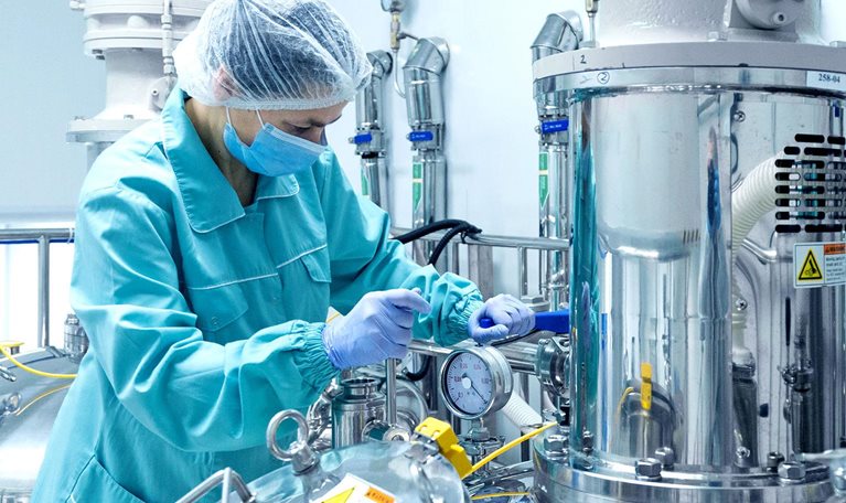 A woman wearing protective clothing operating production line in a sterile environment at a pharmaceutical factory