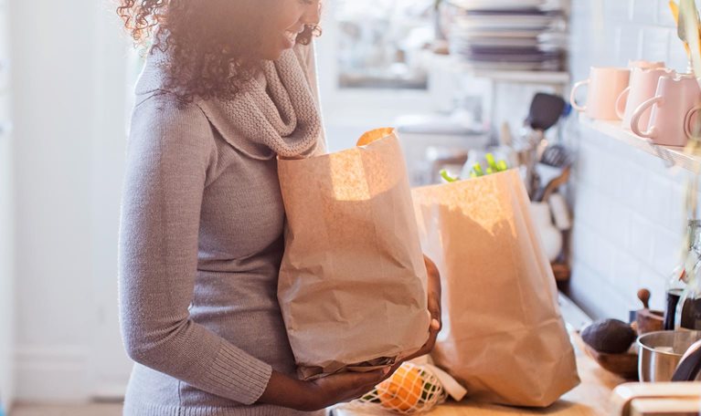 Mother and daughter unloading groceries in sunny kitchen - stock photo