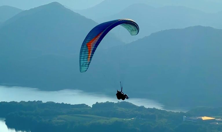A person paraglides on high mountains overlooking the lake
