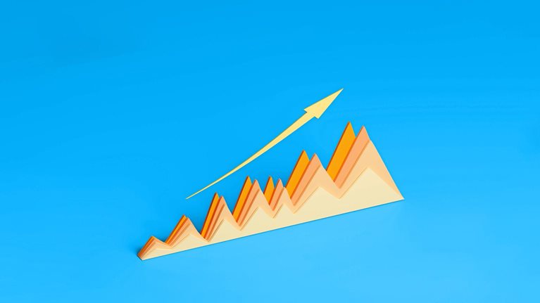 A three-dimensional graph made of paper displays a positive trend with its peaks and valleys. A gold arrow follows the upward trajectory of the graph against a vibrant blue background.