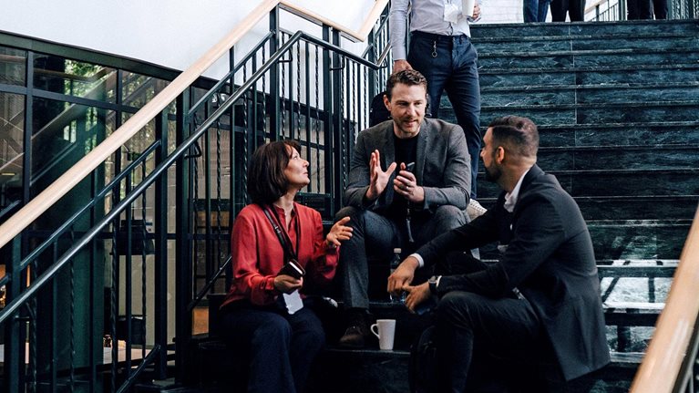 Two men and a woman sitting on the staircase landing engaged in a discussion