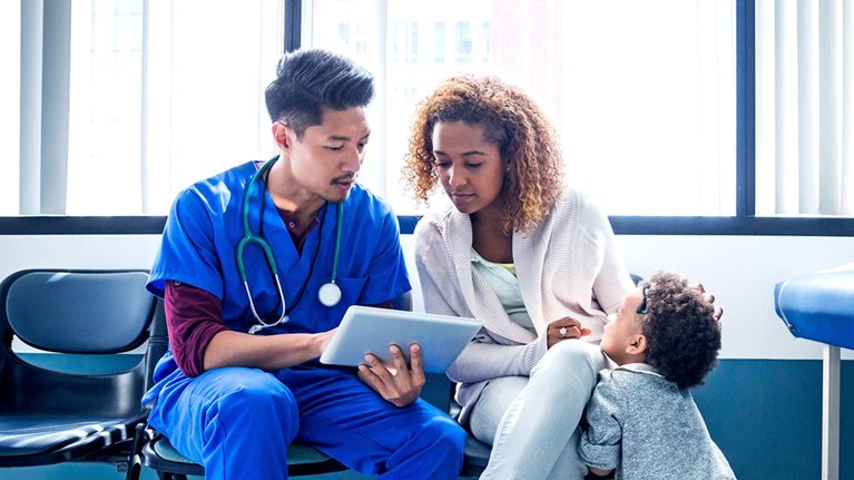 Male nurse showing digital tablet to mother with toddler in hospital