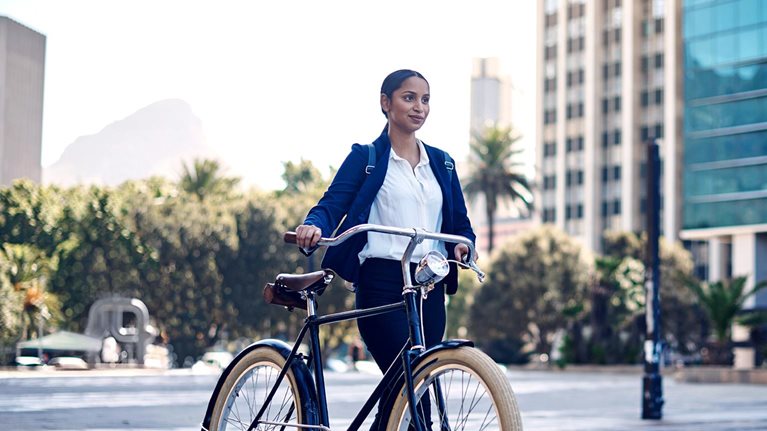 A young South African businesswoman walking her bicycle through a modern downtown. Table mountain is seen in the distance.