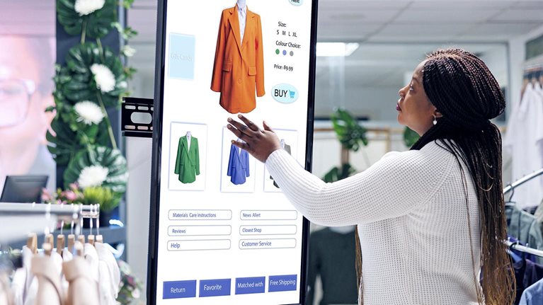 Image of a woman selecting clothes using an interactive touch screen monitor in a clothing store.