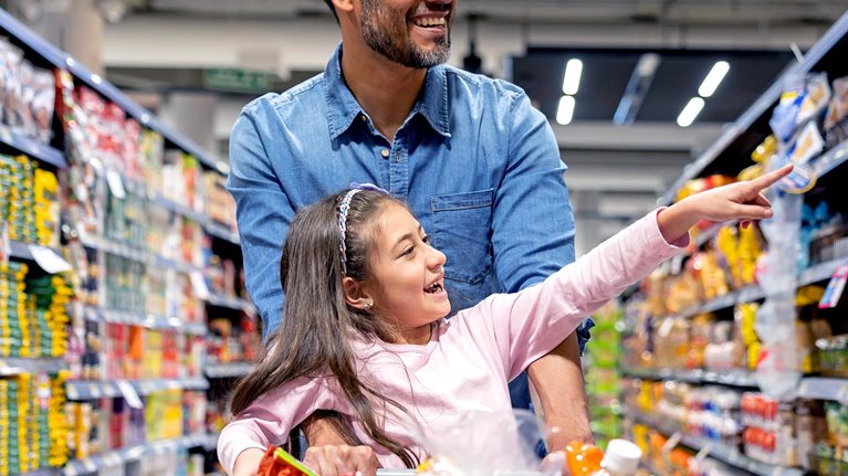 Happy Latin American girl shopping with her father at the supermarket and pointing away at a shelf