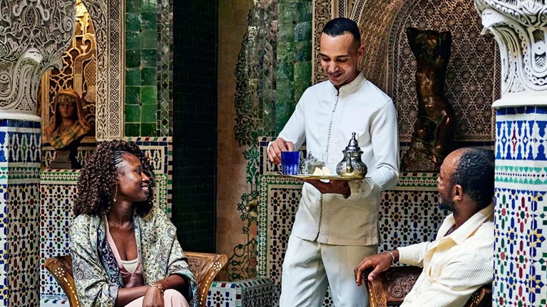 Smiling couple being served tea by concierge in courtyard of luxury hotel while on vacation