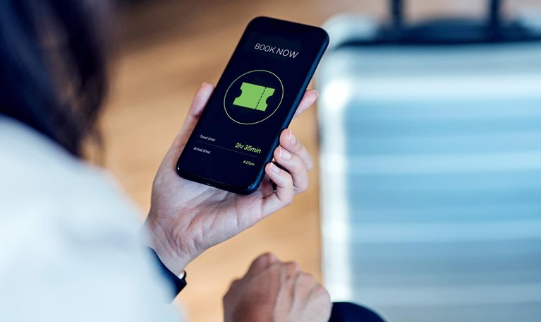Image of a person purchasing a ticket on a mobile device with a suitcase in the background.
