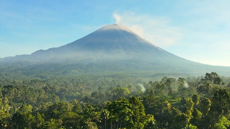 Scenic aerial view sunrise scene of Tumpak Sewu waterfall with Semeru Volcano Background with the jungles on Java Island, Indonesia.